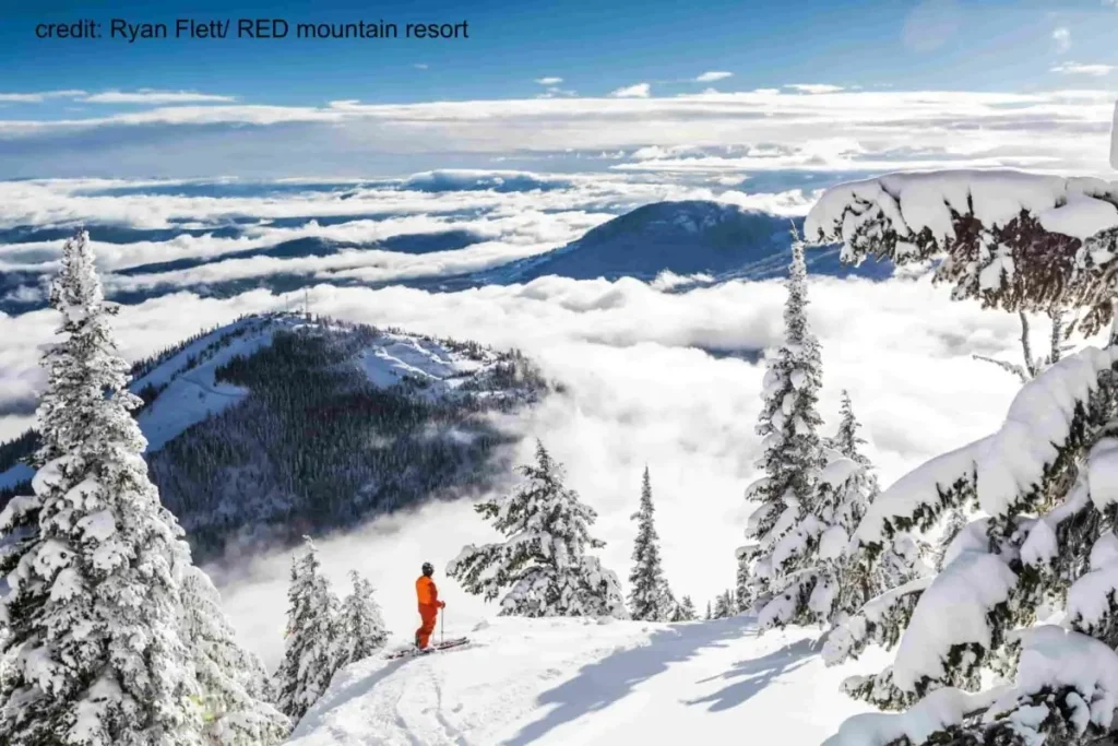 skier looking out over a snowy, cloud topped Red Mountain ski resort
