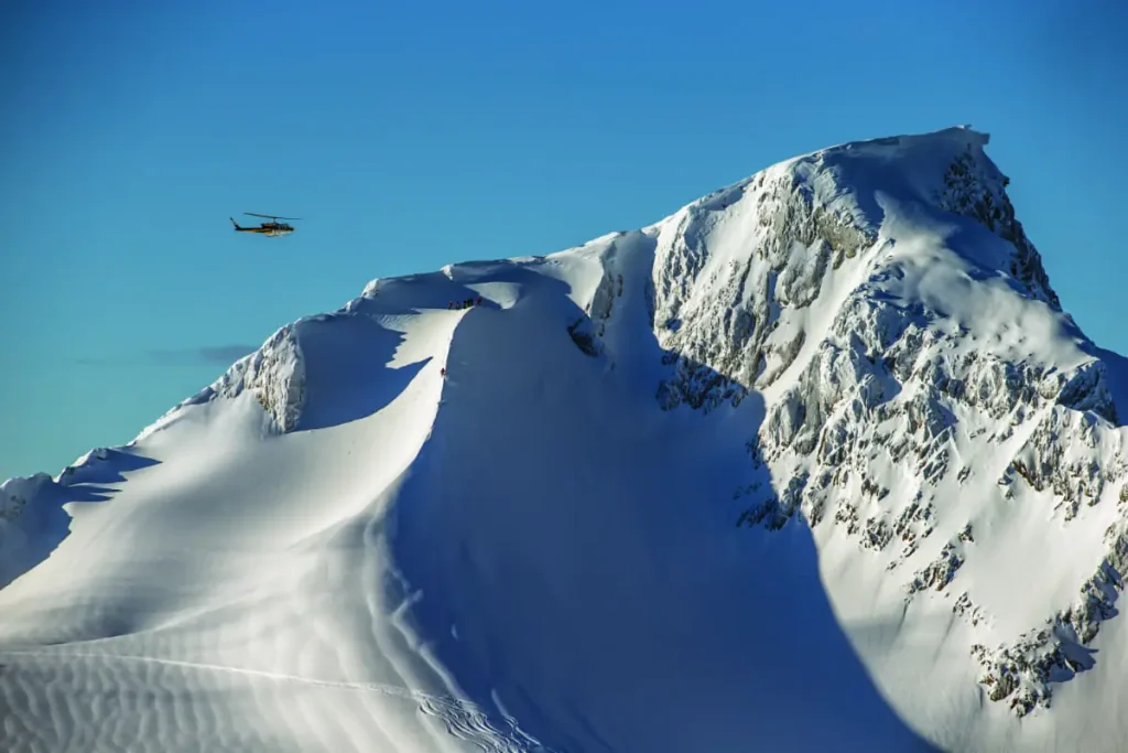 helicopter leaving heli skiers atop a snowy peak