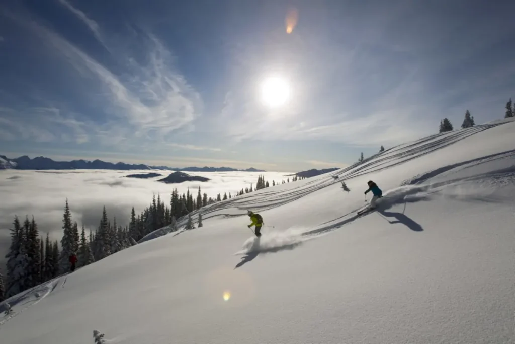 2 skiers above the clouds on a sunny day with Mike Wiegele heli skiing